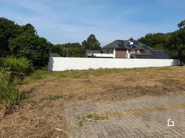 Fachada de uma residência com muro branco e terreno gramado à frente.