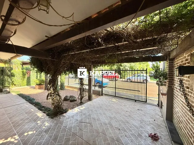 Área externa pavimentada sob uma estrutura coberta com vegetação.