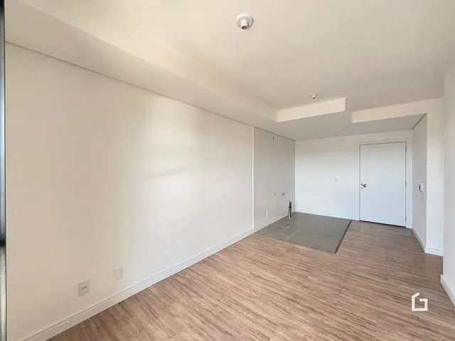 Ambiente interno de uma sala com piso de madeira clara e paredes brancas.