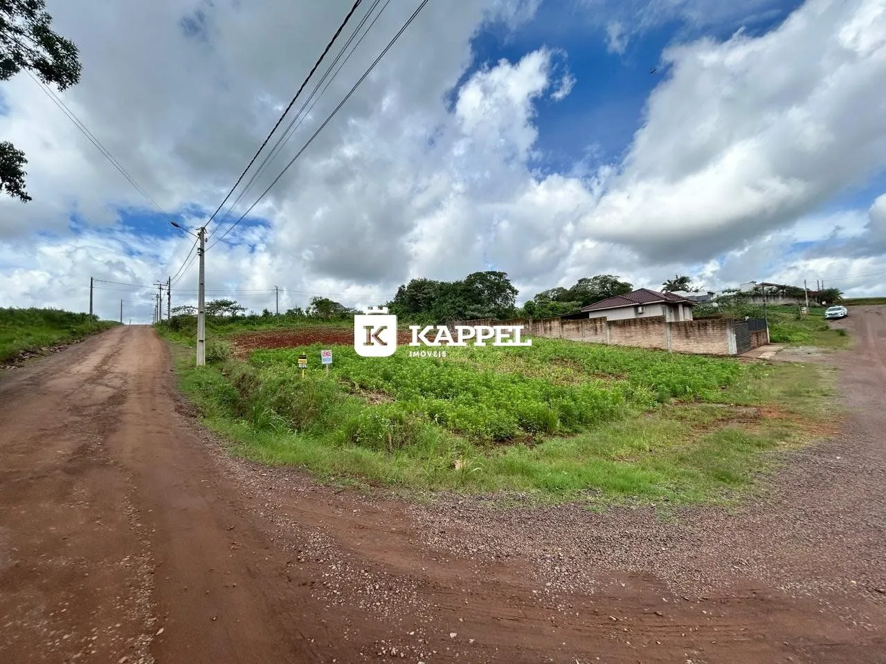 Vista externa de uma estrada de terra que leva a uma residência em uma área rural.