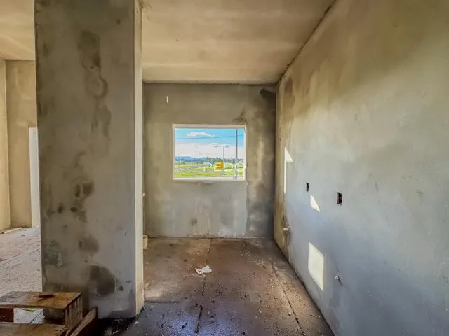 Interior de um cômodo com paredes de concreto cru e uma janela.