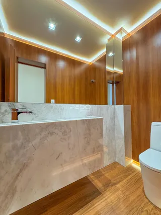 Banheiro com bancada de mármore e revestimento de madeira no ambiente.