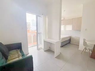 Sala de estar com sofá e porta de vidro que dá acesso a uma varanda.