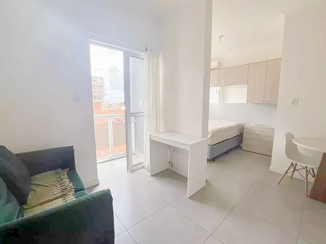 Sala de estar com sofá e porta de vidro que dá acesso a uma varanda.