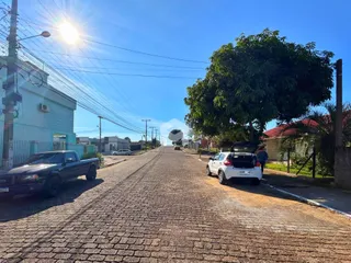 Vista de uma rua pavimentada em Lajeado, Brasil, com árvores e veículos estacionados.