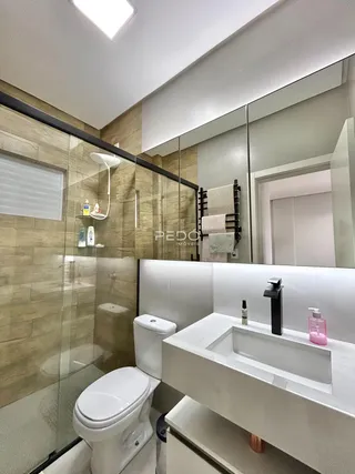 Banheiro moderno com box de vidro e bancada branca.