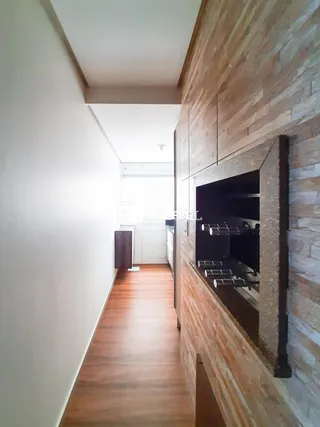 Corredor interno com piso de madeira e área de cozinha com armários em Lajeado.
