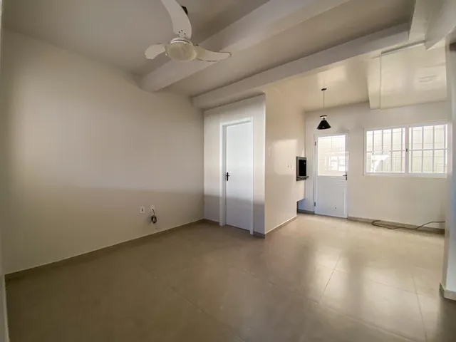 Foto de uma sala ampla e vazia com paredes brancas e piso claro.