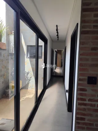 Corredor interno de uma residência com portas de vidro e parede de tijolo aparente.