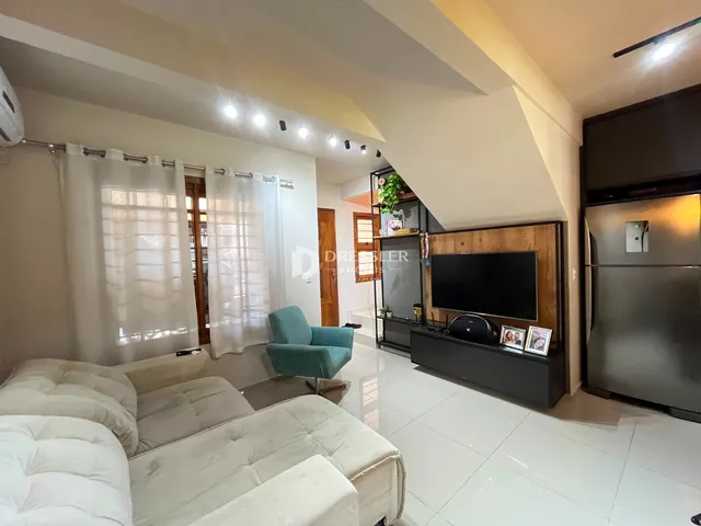 Sala de estar com sofá branco e janelas claras em um imóvel no Brasil.