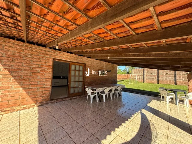 Vista de uma área externa coberta com piso de cerâmica e mesa de jantar.