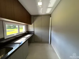 Vista de uma cozinha com bancada e janela para um campo aberto.