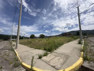Vista externa de um caminho de concreto com vegetação alta no fundo sob um céu parcialmente nublado.