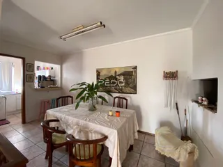 Uma sala de jantar com mesa coberta e pintura na parede branca.