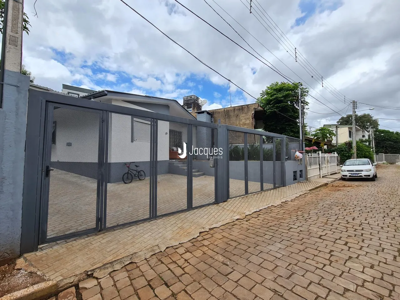 Vista externa de uma propriedade com cerca de metal e pavimento de tijolos.