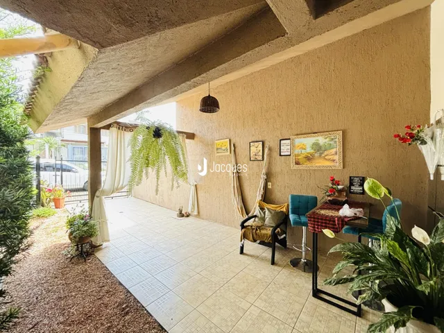Área externa coberta com piso de cerâmica e decoração de plantas.
