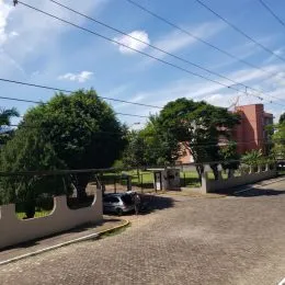 Vista externa de uma propriedade com árvores e uma cerca branca no ambiente.