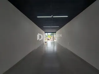 A foto mostra um corredor longo com paredes brancas e piso claro.