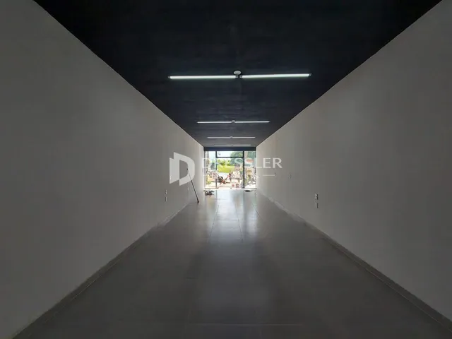 A foto mostra um corredor longo com paredes brancas e piso claro.