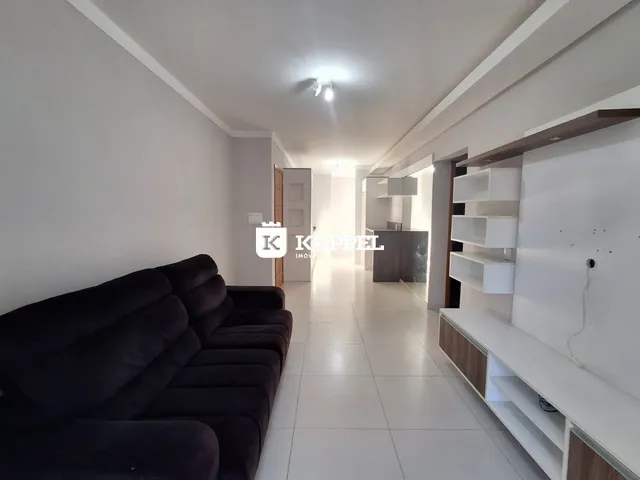Hall de entrada com sofá escuro e estantes brancas em um apartamento.