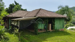 Fachada de uma casa verde com telhado de telhas cercada por vegetação.