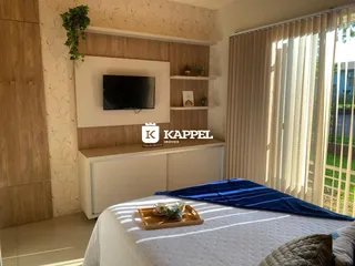 Quarto com cama e painel de TV montado na parede, com luz natural entrando pela janela.