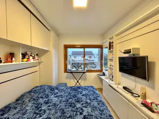 Quarto interno com cabeceira e armários brancos.