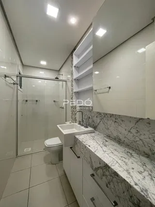 Foto de um banheiro com revestimento em mármore e box de vidro.