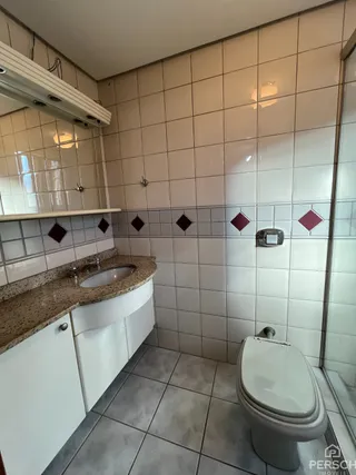Banheiro com revestimento de azulejos brancos e louças sanitárias.