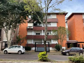 Vista externa de um prédio residencial em Lajeado, Brasil, com árvores e veículos estacionados na rua.