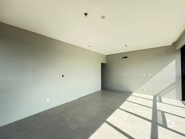 Interior de uma sala ampla com paredes brancas e piso cinza.