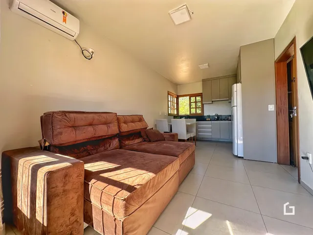 Sala de estar com sofá e cozinha visíveis no fundo da imagem.