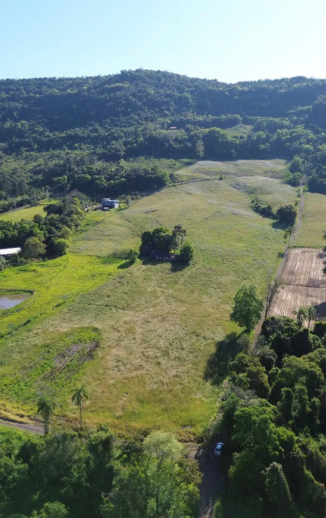 Vista aérea de uma área rural com campos gramados e vegetação densa.