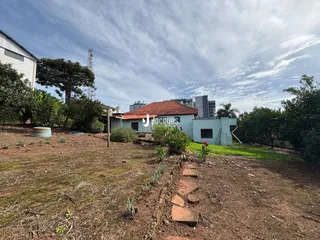 Vista externa de um terreno com vegetação seca e uma construção ao fundo.