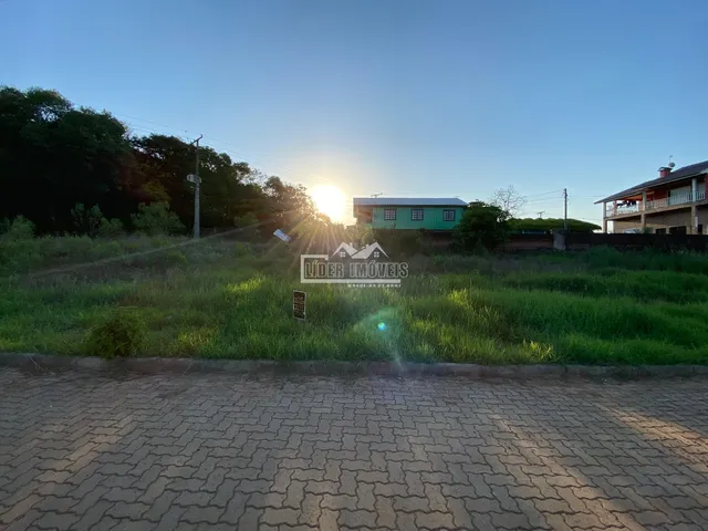 Vista externa de uma propriedade com campo gramado e vegetação ao pôr do sol.