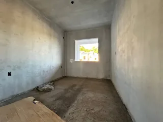 Vista interna de um corredor com paredes brancas e piso de concreto.