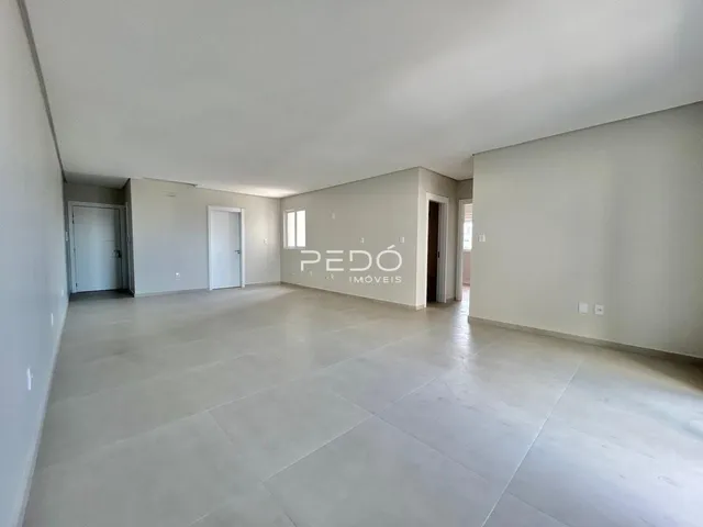 Interior de uma sala ampla com piso claro e paredes brancas.