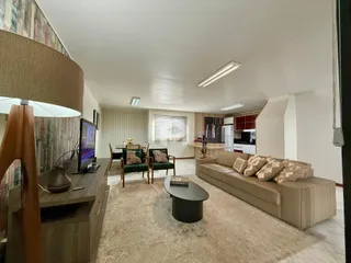 Sala de estar com decoração moderna e área de cozinha ao fundo.