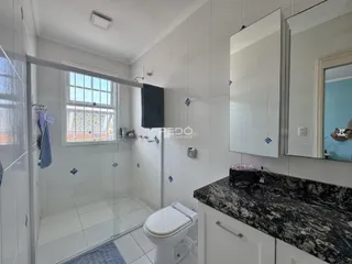 Banheiro com box de vidro e revestimento branco.