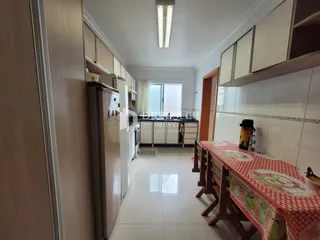 Vista interna de uma cozinha com armários brancos e mesa de jantar em Lajeado.