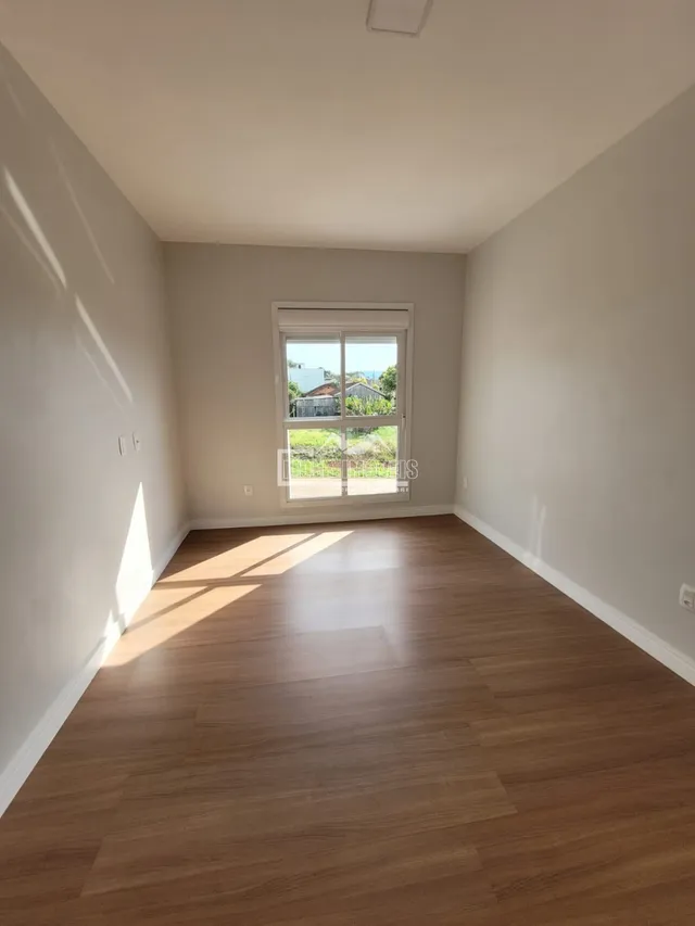 Ambiente interno de uma sala com piso de madeira clara e paredes brancas.