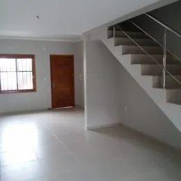 Sala de estar ampla com piso claro e escadaria visível na área interna da residência.