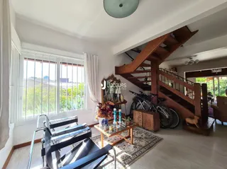 Interior de uma sala com escadaria de madeira e grandes janelas.