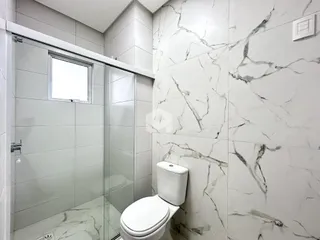 Banheiro com box de vidro e revestimento de mármore nas paredes.