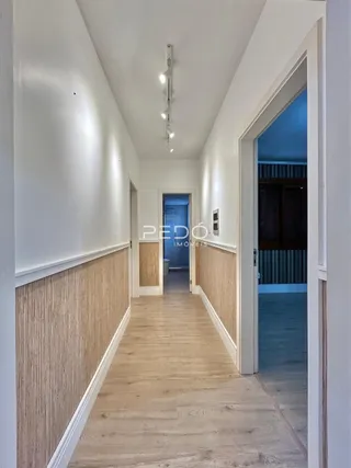 Corredor interno de uma residência com piso de madeira clara.