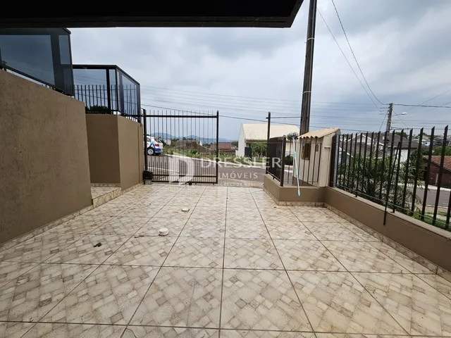 Área externa pavimentada com piso de cerâmica e portão de ferro.