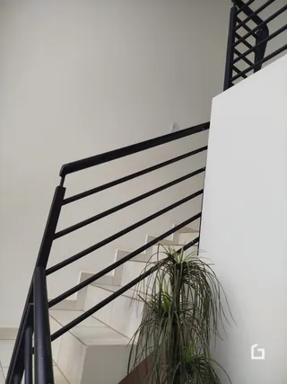 Vista de uma escadaria interna com corrimão preto e paredes brancas.