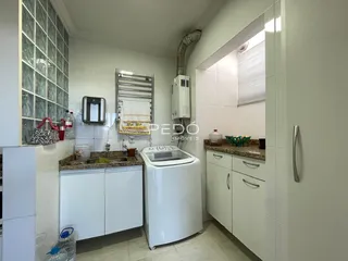Interior de uma área de serviço com máquina de lavar e bancada em cerâmica branca.