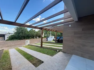 Vista externa de uma casa com estrutura de pérgola e área externa pavimentada.