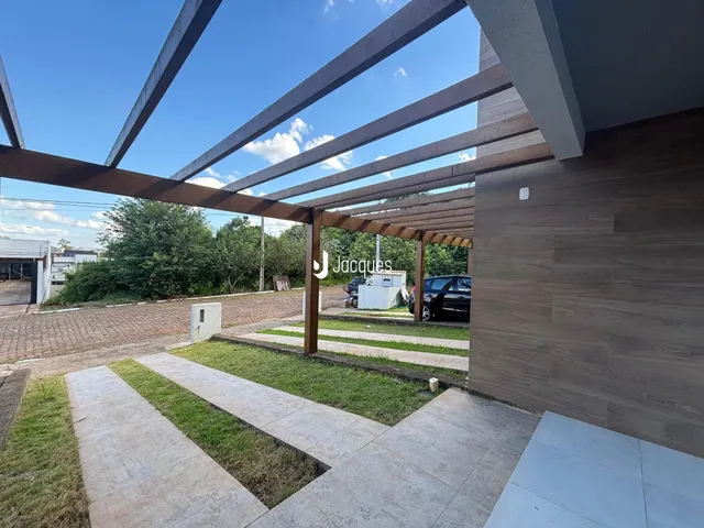 Vista externa de uma casa com estrutura de pérgola e área externa pavimentada.